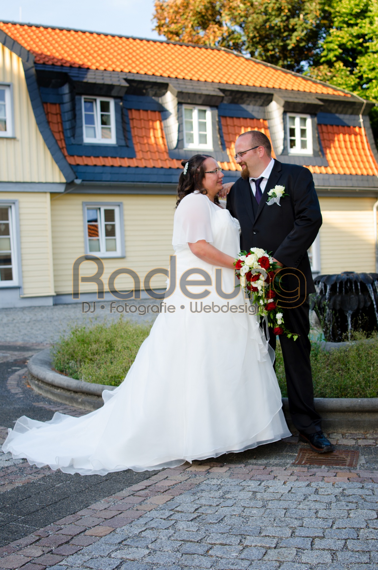 Ein Brautpaar steht auf einem Hof vor einem Brunnen und schaut sich verliebt an